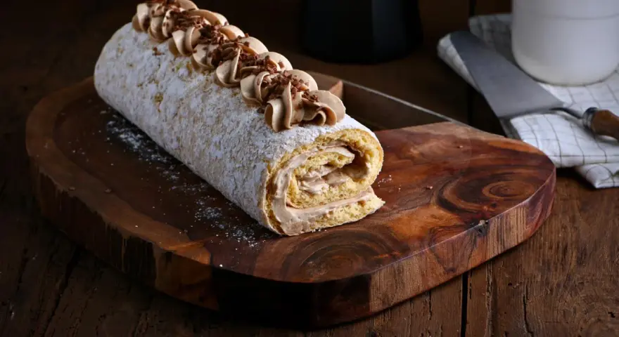 Un delicioso brazo de gitano cubierto de azúcar glas y decorado con crema de café y virutas de chocolate, listo para ser servido.