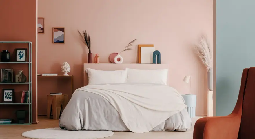 Camera da letto moderna con letto king-size, biancheria grigia e coperta color crema. Idee per come abbellire una camera da letto con decorazioni astratte e piante.