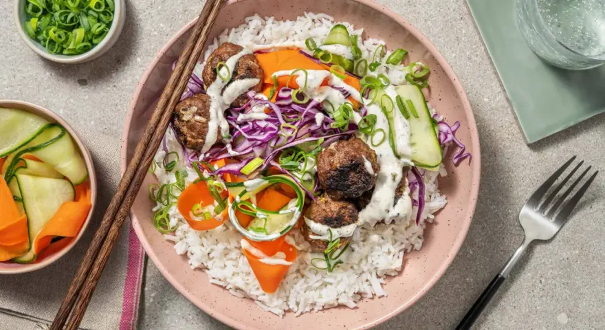 En skål med ris, köttbullar, strimlad rödkål, morötter och gurka, toppad med en krämig sås. En härlig vietnamesisk matupplevelse.