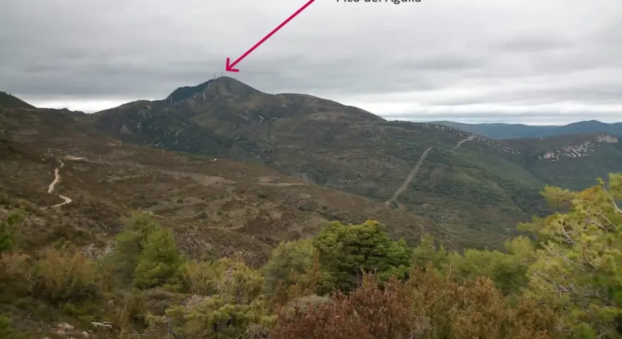 Un sendero serpentea hacia el **Pico del Águila**, coronado por antenas, bajo un cielo nublado.