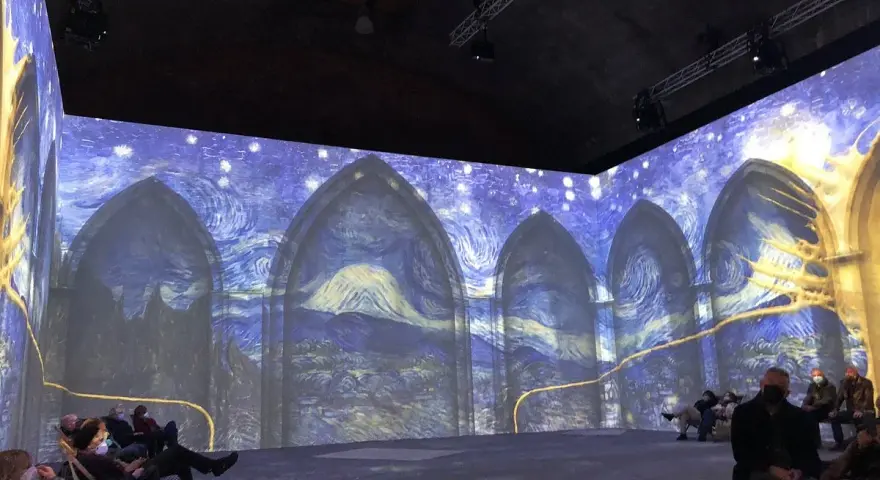 En uppslukande utställning där Van Goghs konstverk projiceras på väggarna, vilket ger en känsla av att van Gogh är levande. Besökare sitter och njuter av den visuella upplevelsen.