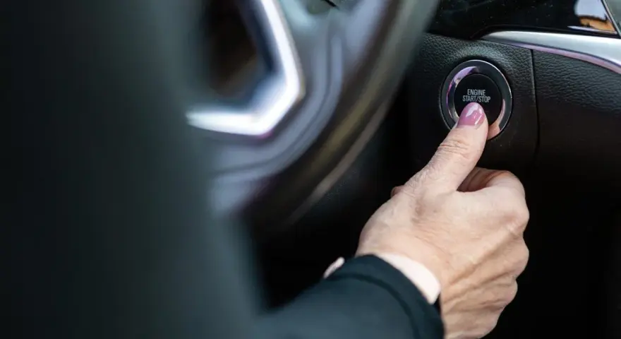 Dłoń naciska przycisk "ENGINE START/STOP". Niestety, samochód nie odpala, co frustruje kierowcę.