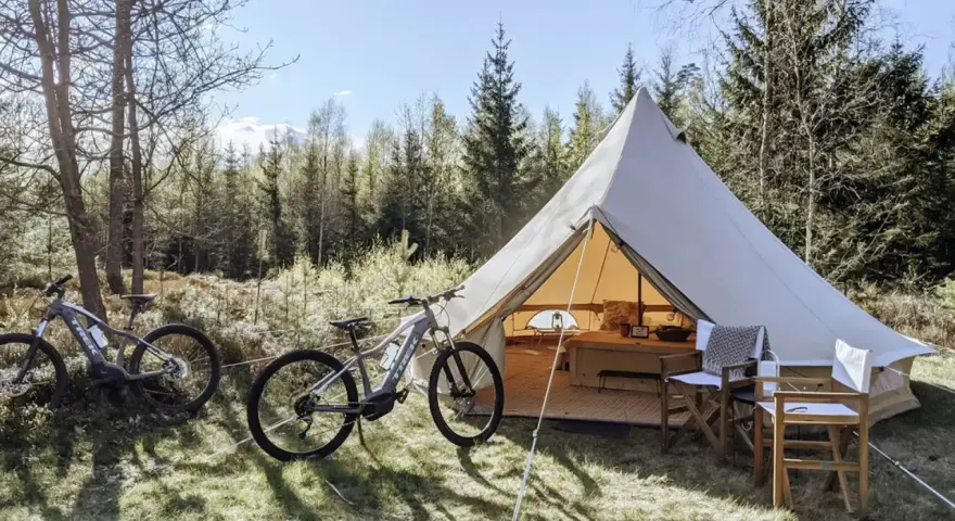 Två elcyklar står redo för äventyr vid ett stort tält på Bengts camping. Skogen bakom bjuder in till utforskning.