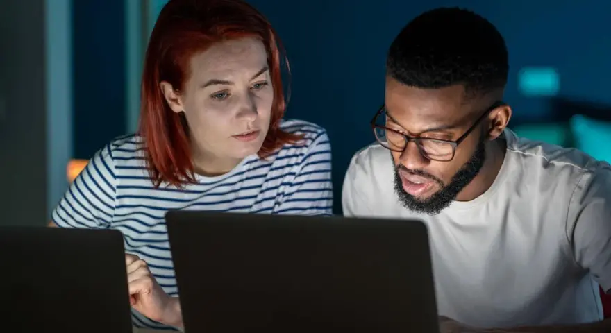 Zwei Personen arbeiten konzentriert an Laptops. Sie besprechen Details, vielleicht für einen partnerschaftsvertrag ohne notar.