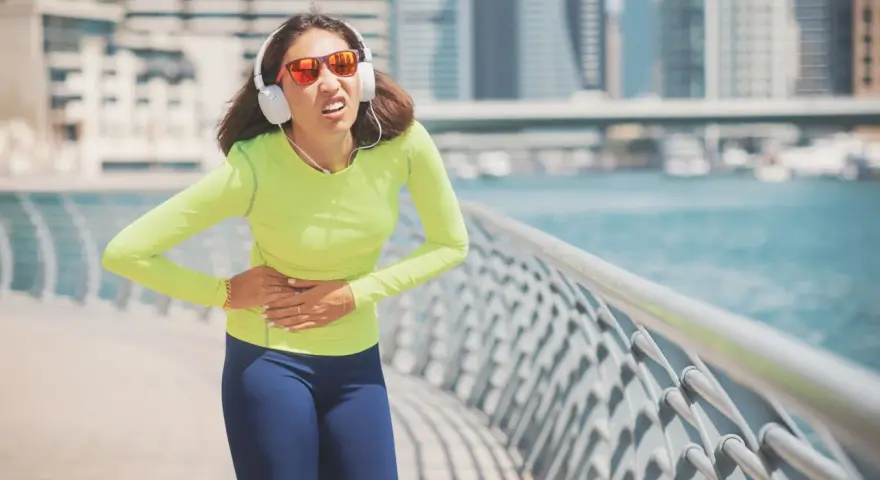 Une coureuse en tenue de sport, écouteurs aux oreilles, se tient le ventre, visiblement prise d'un point de côté.