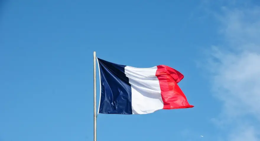 Die französische Flagge weht im Wind vor blauem Himmel. Ein Symbol für ein spannendes Auslandsjahr in Frankreich.