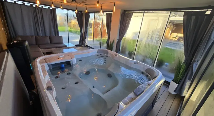 Relaks w jacuzzi pod ciepłym światłem lamp w przeszklonym tarasie zimowym. Obok wygodna sofa i stolik.