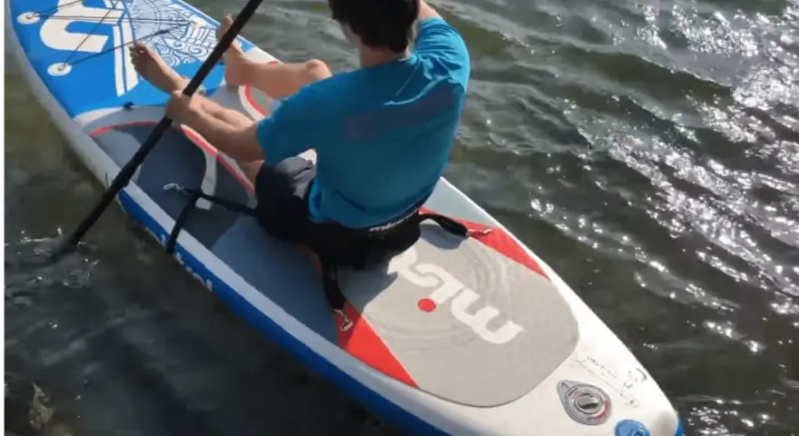 Mann sitzt auf SUP-Board, paddelt und befestigt den Sitz.