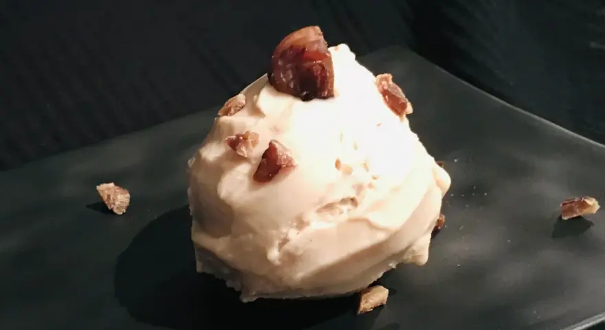 Cremiges Maronen Eis, garniert mit kleinen Maronenstückchen, auf einem dunklen Teller. Ein Genuss für kalte Tage.