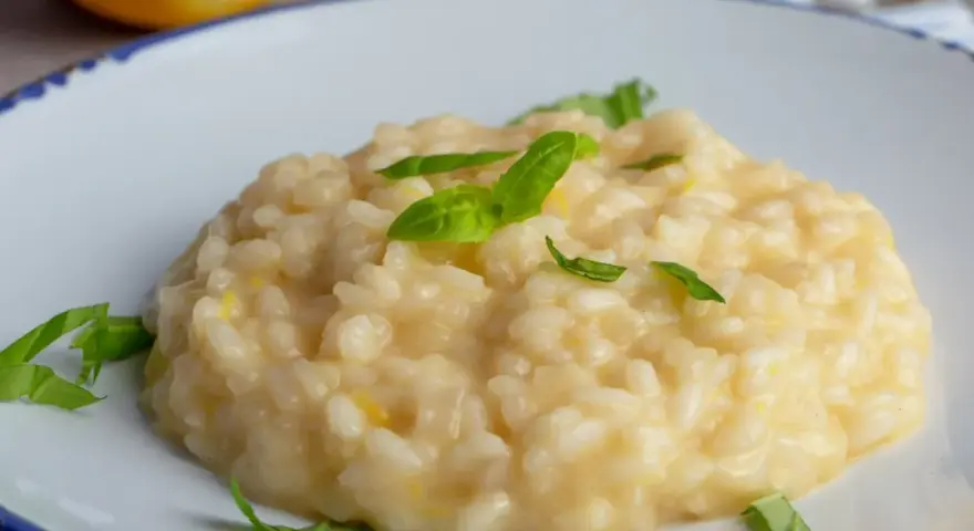 Kremowe, letnie risotto z cytryną i bazylią, podane na białym talerzu z niebieskim rantem.