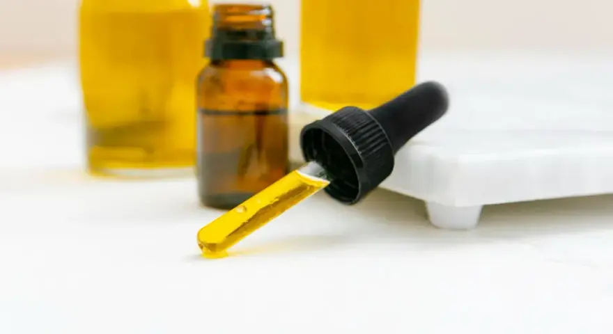 Kropla olejku z pipety, obok buteleczek z żółtym płynem. Czy to patchouli?