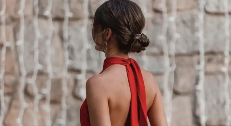 Elegante moño bajo en una mujer con vestido rojo, luciendo su espalda descubierta y un pendiente llamativo.