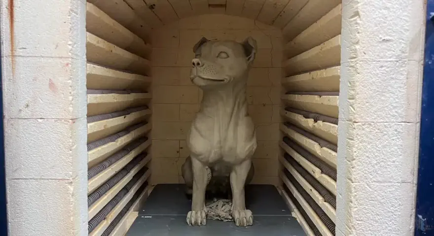En hundskulptur i blålera keramik väntar på att brännas i en ugn.