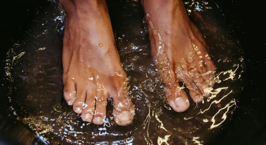 A close-up of feet soaking in a dark basin, likely a relaxing foot bath with epsom salt for feet.