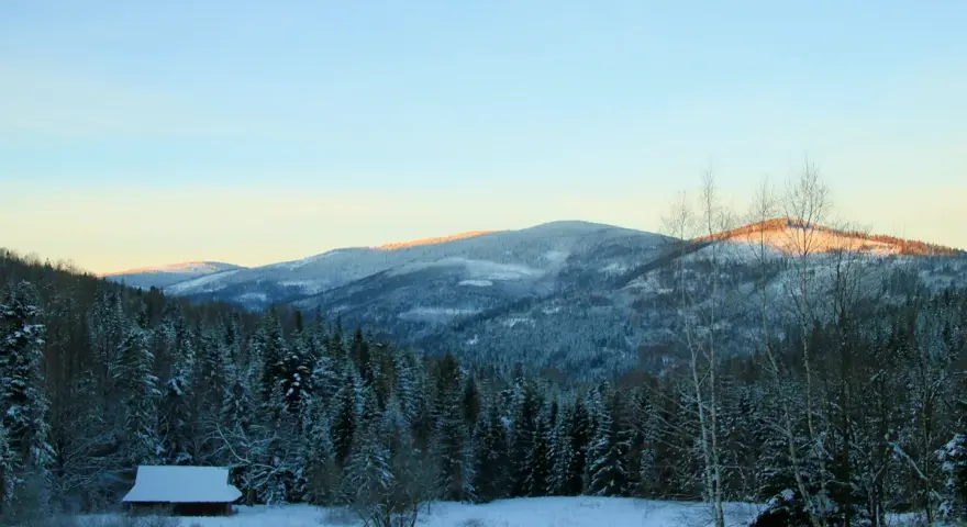 Zimowy krajobraz z chatką i lasem iglastym. W oddali ośnieżone góry, przez które biegnie rysianka szlak z Sopotni.