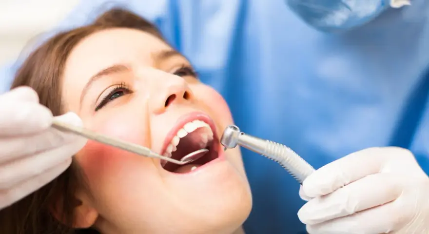 Pacjentka u dentysty, który bada jej usta. Widoczne narzędzia stomatologiczne i zaczerwienione dziąsło, sugerujące ropne zapalenie dziąseł.