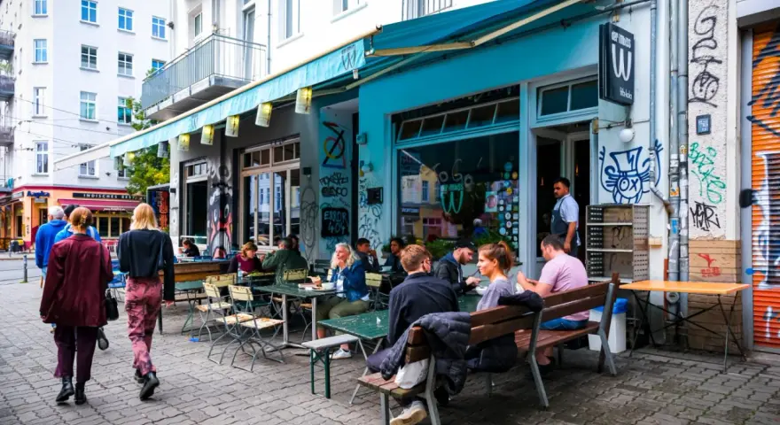 Menschen sitzen an Tischen vor einem **Prenzlauer Berg Restaurant** mit türkisfarbener Markise und Graffiti.
