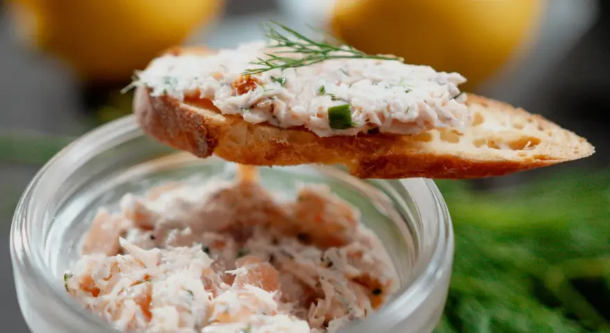 Un toast garni de rillettes de saumon, décoré d'aneth, avec un pot de rillettes en arrière-plan.