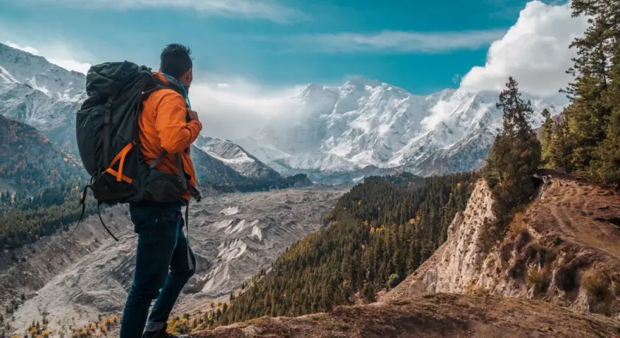 Wędrowiec z plecakiem podziwia majestatyczne, ośnieżone szczyty. Widok przypomina baśniowe polany, gdzie natura ukazuje swoje surowe piękno.