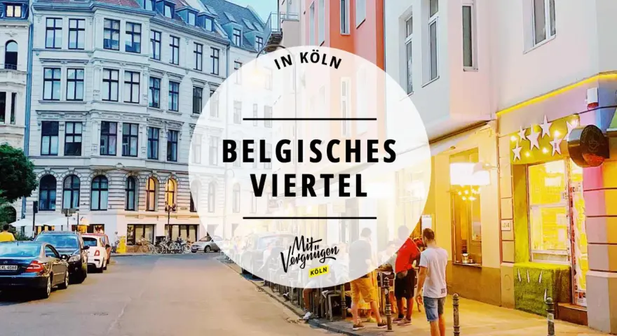 Abendstimmung im Belgischen Viertel in Köln. Menschen sitzen vor beleuchteten Geschäften, Autos parken am Straßenrand.