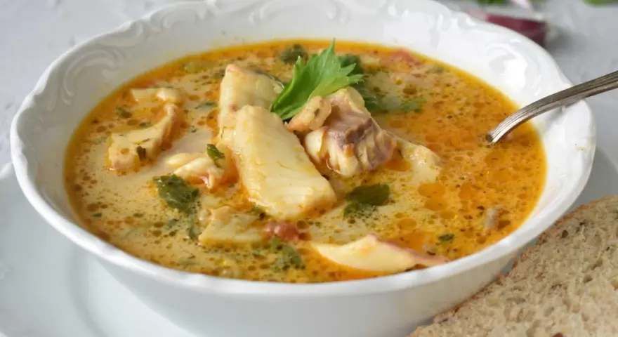 Sopa de pescado casera en un cuenco blanco con trozos de pescado, perejil y una rebanada de pan.