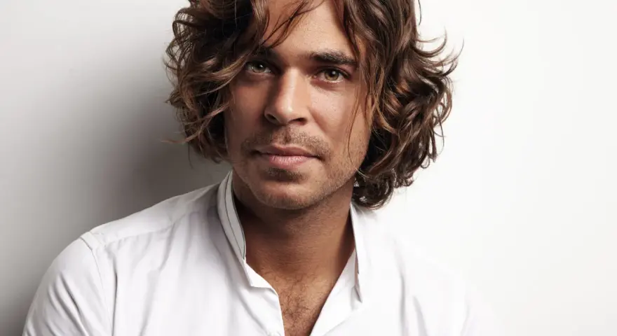 Hombre con cabello castaño ondulado, un ejemplo de cortes de pelo hombre medio largo, viste camisa blanca.