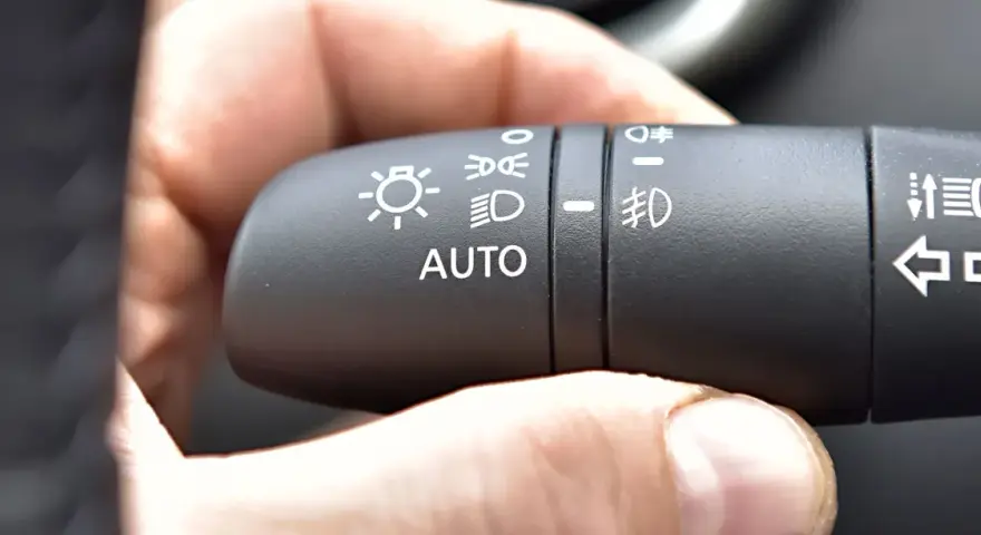 Dłoń naciska przełącznik świateł w samochodzie, wybierając tryb AUTO, który może obejmować światła do jazdy dziennej (DRL).