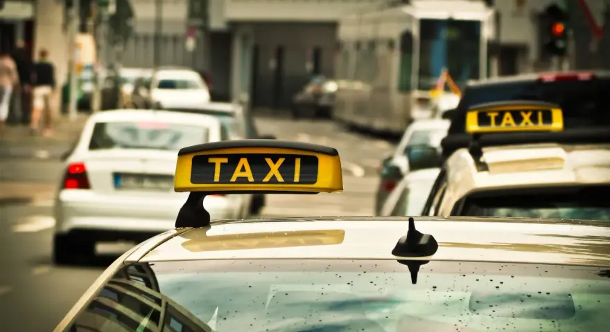 Ein Taxi mit leuchtendem "TAXI"-Schild auf dem Dach, bereit für Fahrten, auch im nachttarif. Regentropfen auf der Windschutzscheibe.