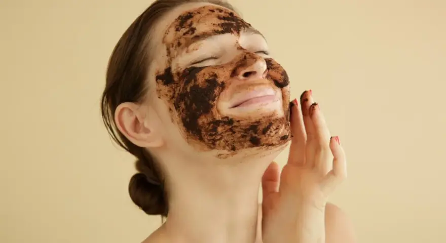 Mujer disfrutando de una mascarilla de café para la cara, con los ojos cerrados y una sonrisa.