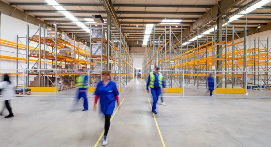 Persone in movimento in un magazzino moderno, con scaffalature piene di merci. Un'immagine che evoca il dinamismo del lavorare come magazziniere.