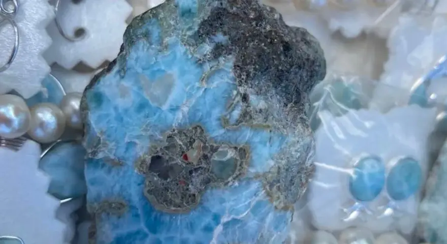 Surowy larimar, kamień o niebiesko-białych żyłkach, otoczony perłami i ozdobami. Jego magiczne właściwości uspokajają i przynoszą harmonię.