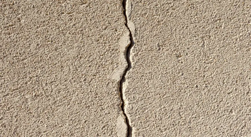 Grosse fissure sur un mur extérieur en crépi. Il faut réparer cette fissure pour éviter qu'elle ne s'aggrave.