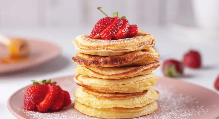 Pancakes dorati, perfetti per una ricetta pancake veloce senza lievito, guarniti con fragole fresche e zucchero a velo.