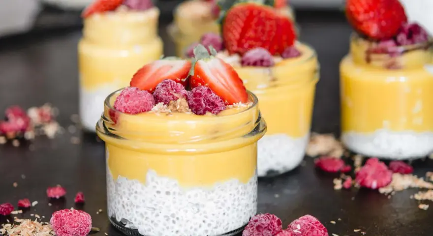 Erfrischender Mango Chia Pudding in Gläsern, garniert mit Erdbeeren und Himbeeren. Ein gesunder Genuss!
