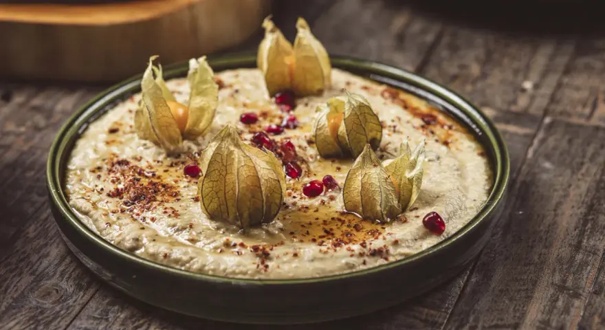 Krämig baba ganoush toppad med physalis och granatäppelkärnor på en rustik träyta.