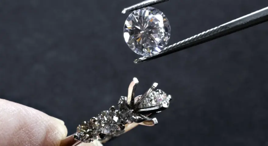 Un diamante viene posizionato con una pinzetta su un anello con incastonatura a castone ribattuto, pronto per essere fissato.