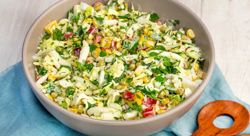 Schüssel mit knackigem Salat aus Weißkohl, Mais, Erbsen und Paprika, perfekt als salate zum vorbereiten am vortag. Mit frischer Petersilie garniert.
