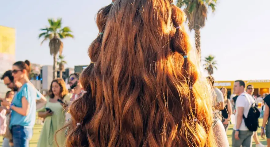 Peinados para festivales: cabello largo y ondulado con secciones recogidas en pequeñas coletas, ideal para disfrutar del sol y la música.