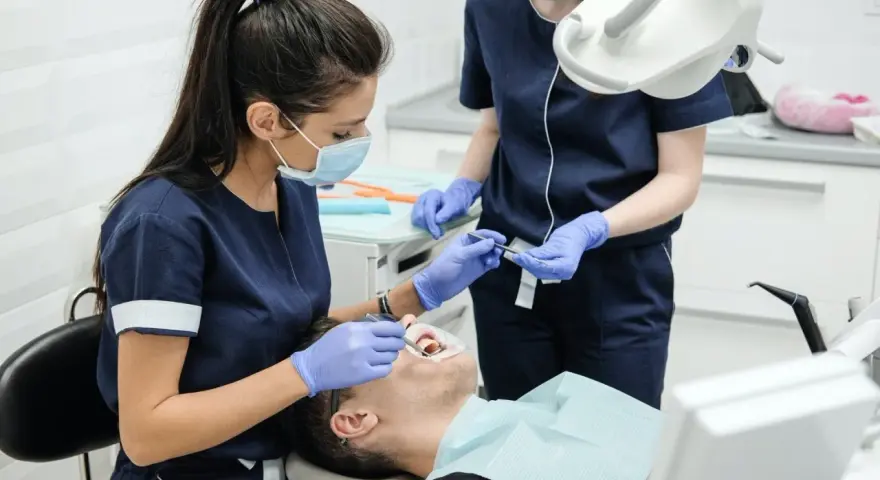 Dwie dentystki w maseczkach i rękawiczkach wykonują zabieg stomatologiczny u pacjenta.