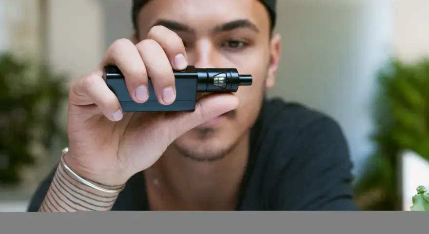 Joven con gorra negra sostiene un cigarrillo electrónico, mostrando sus claromizadores.