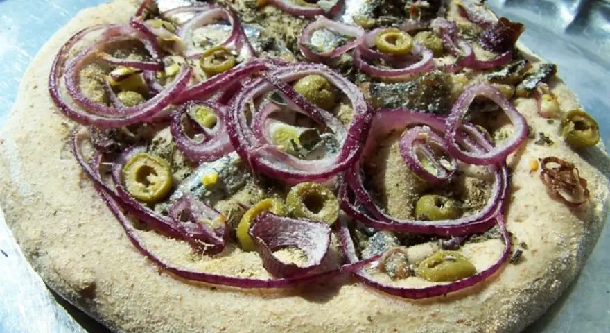 Pizza z anszua, oliwkami i czerwoną cebulą, gotowa do pieczenia.