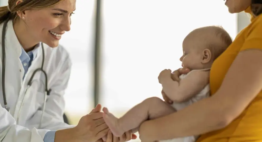 Lekarka bada niemowlę, które może być narażone na adenowirusa u dzieci. Uśmiechnięta lekarka delikatnie dotyka stópki dziecka.