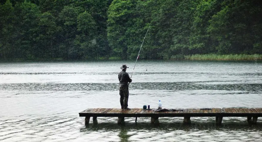 Ein Angler steht auf einem Steg und übt aus, wie angelt man, während es regnet.
