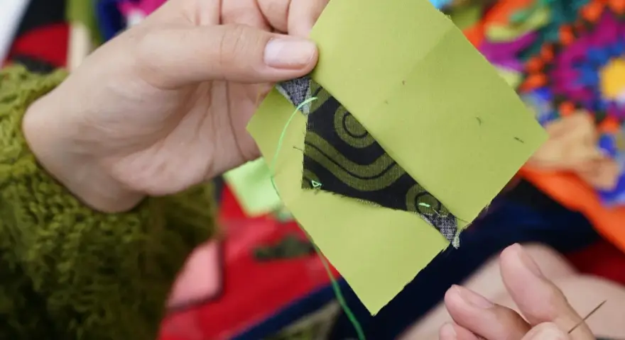 Ręce szyją zielone kwadraty z czarnym wzorem, tworząc patchwork projekty.