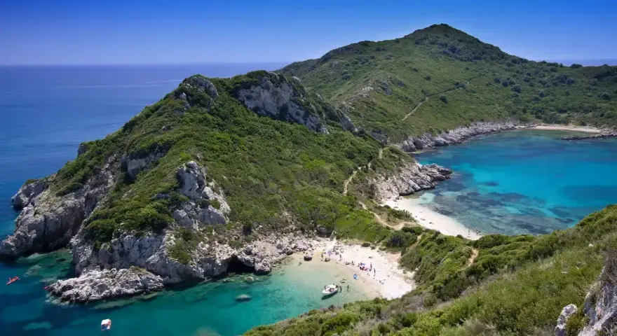 Malownicza zatoka z turkusową wodą i piaszczystą plażą, otoczona zielonymi wzgórzami. Tak właśnie wygląda Korfu, grecka wyspa, gdzie leży ten raj.