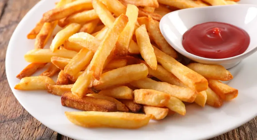 Une assiette de frites au four dorées et croustillantes, accompagnées d'un petit bol de ketchup rouge vif.