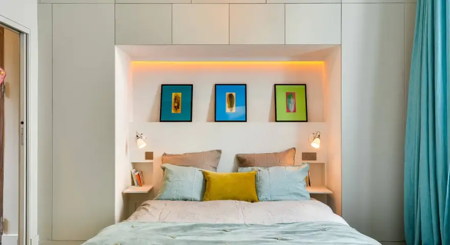 Idee salvaspazio camera da letto piccola: letto con testiera contenitore, quadri colorati e tende turchesi creano un ambiente accogliente.