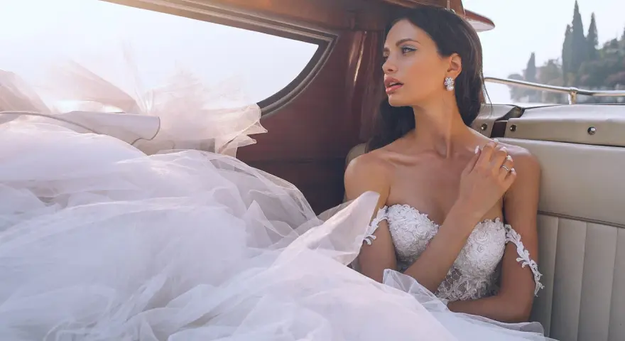 Sposa con abito bianco e trucco impeccabile, seduta su una barca, con il velo che ondeggia al vento.