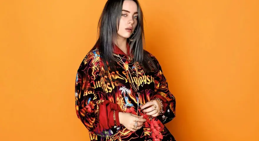 Billie Eilish w kolorowej bluzie, z mnóstwem złotych łańcuchów i pierścionków, jakby przygotowywała się do odebrania kolejnych nagród.