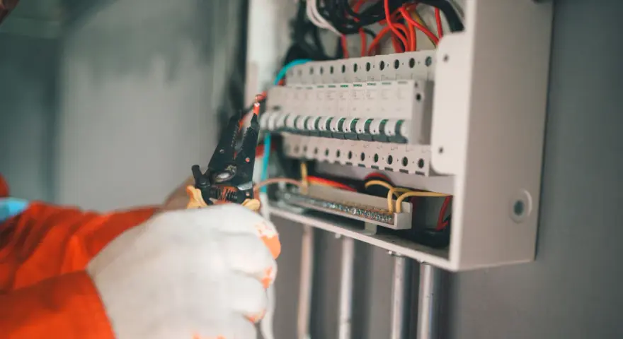 Elektryk w białych rękawicach wywala bezpiecznik w skrzynce, używając szczypiec.
